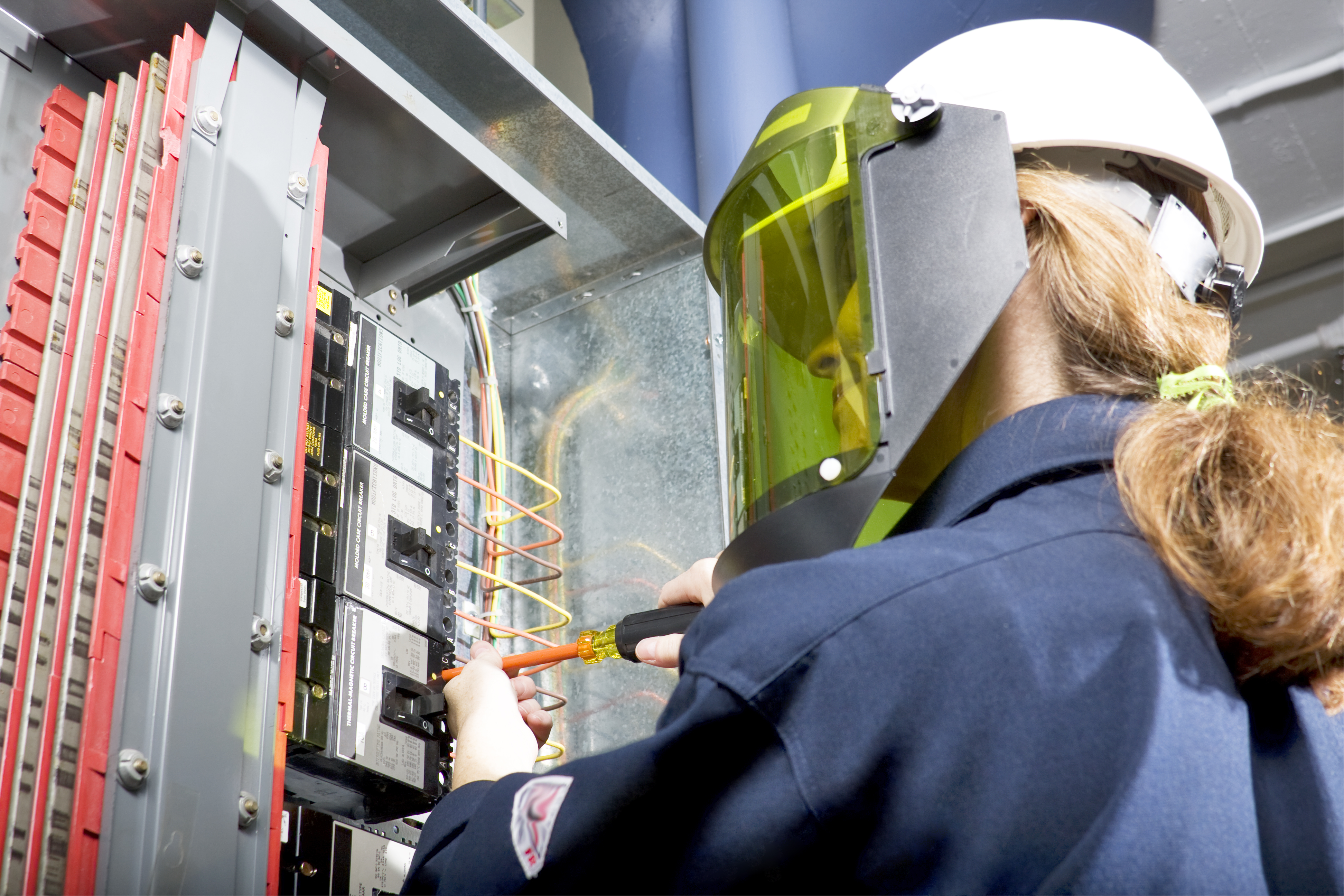 woman wearing a face mask to protect herself from electrical shocks while inspecting a electrical panel.