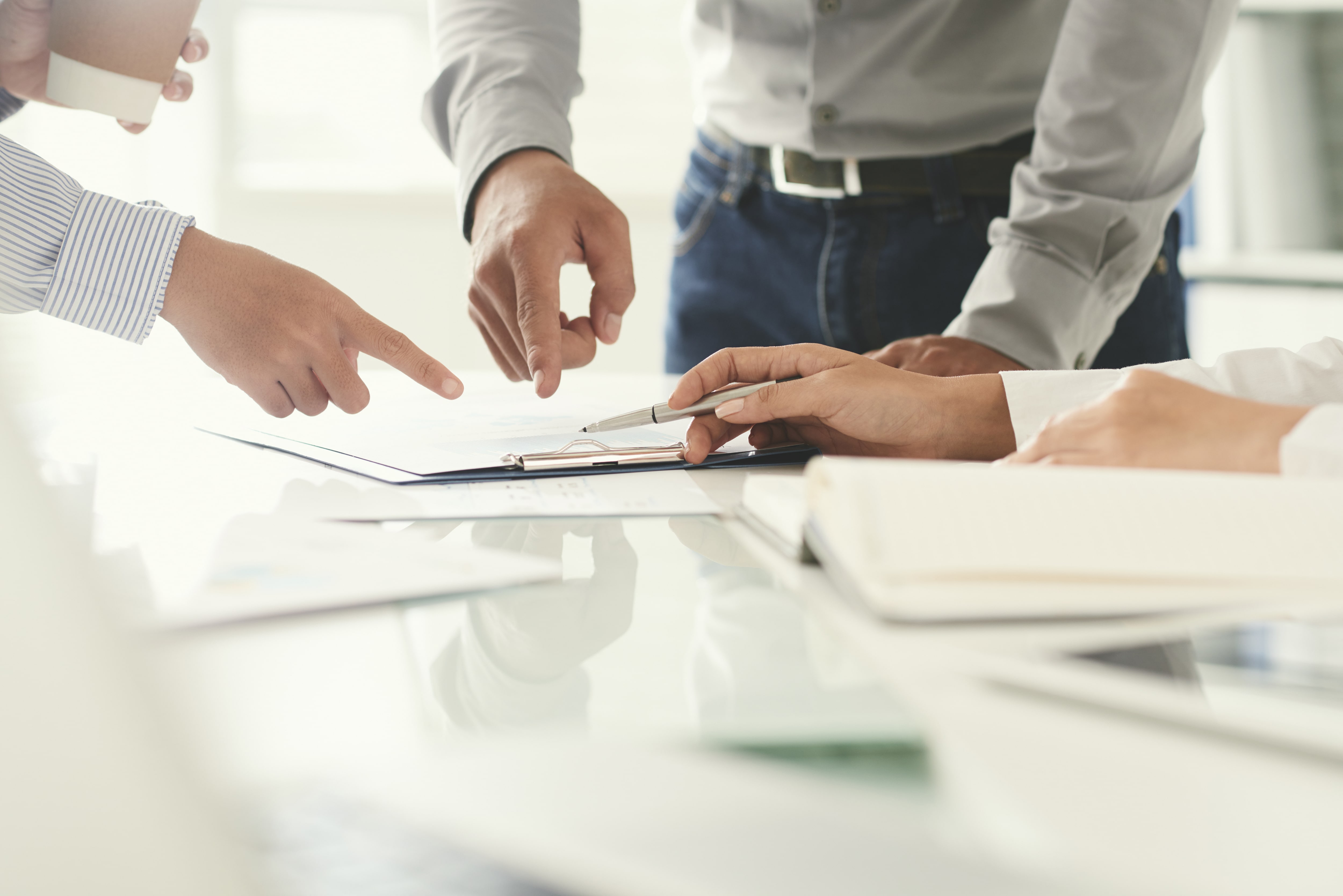 close up of a clipboard on a table with multiple hands pointing at it