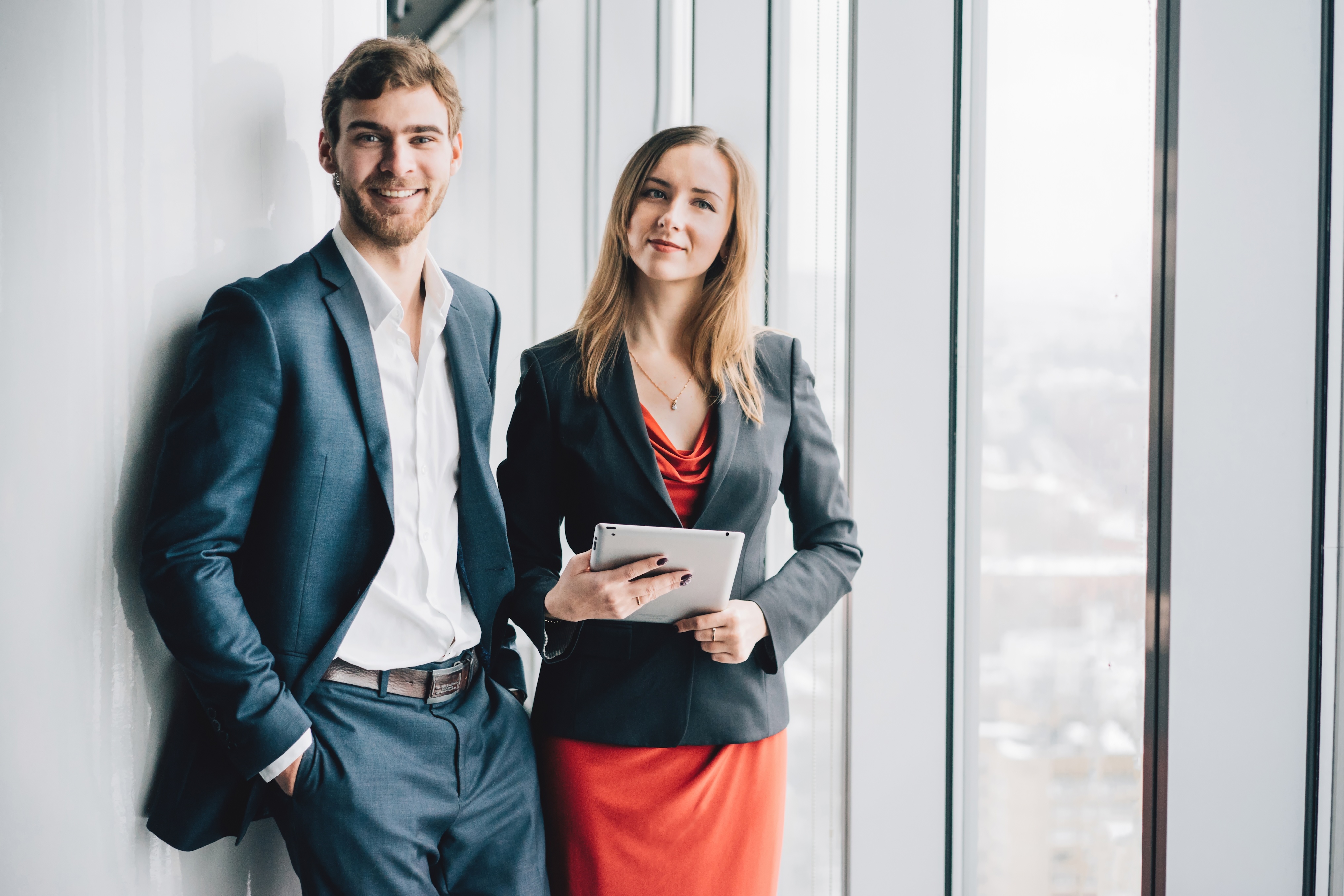 Group of business people, a man in a suit and a woman in a red dress and jacket, holding a tablet, winter city landscape outside the window on the background