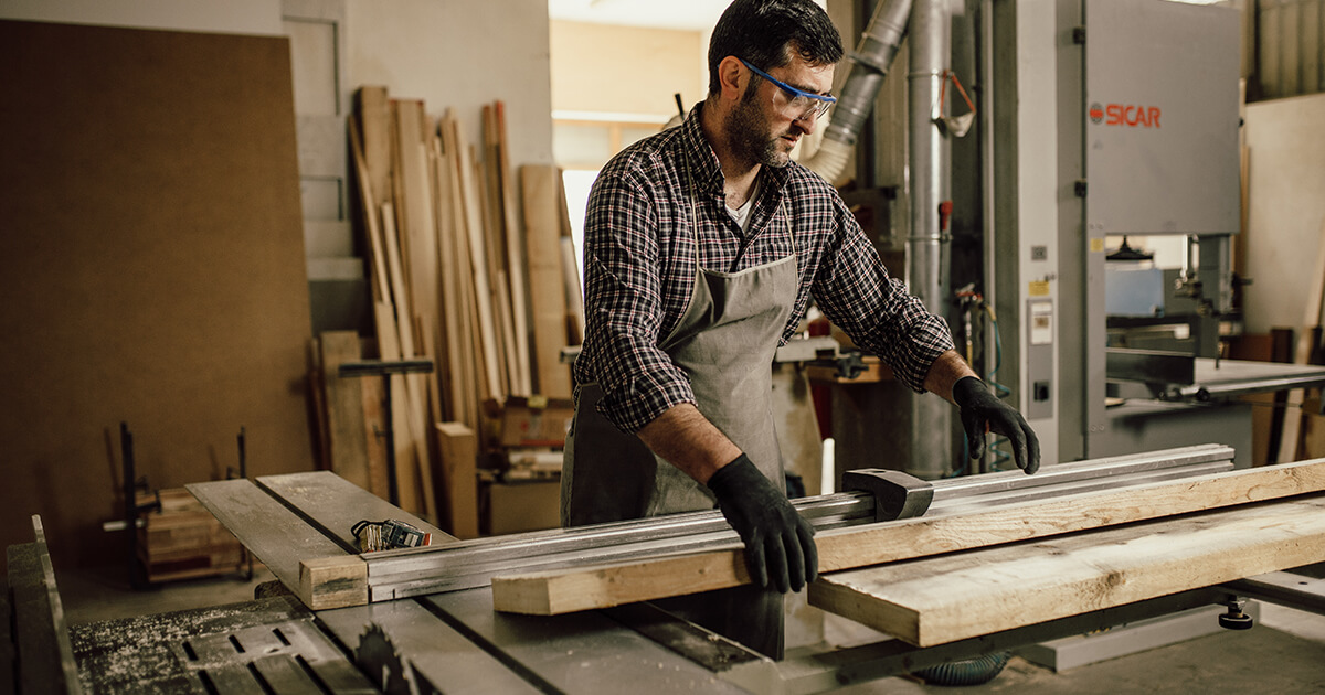 man wearing safety glasses and gloves using a table saw to cut wood