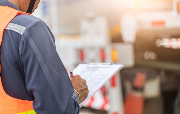 Worker in a high visibility vest holding clipboard checking items off on a checklist with a pen