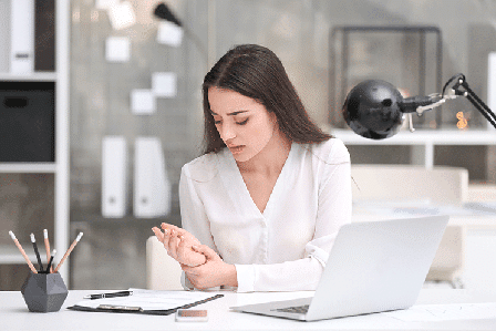 Woman holding wrist in pain beside laptop
