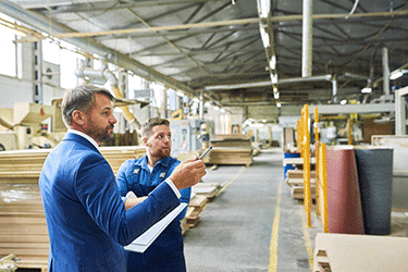 Man wearing suit with clipboard inspecting warehouse with worker