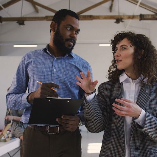 Two happy young multiethnic man and woman, corporate business managers walk along modern loft office talking informally.